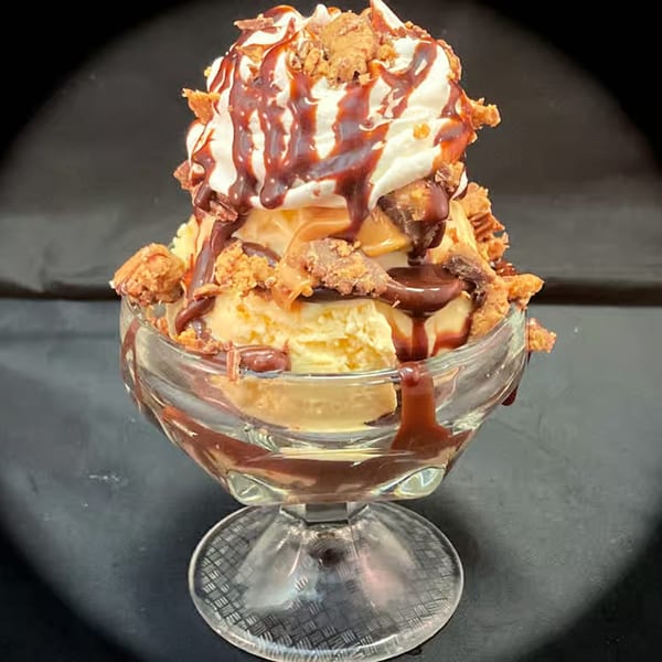 Vanilla ice cream sundae with whipped cream, chocolate syrup, and peanut butter candy crumbles.