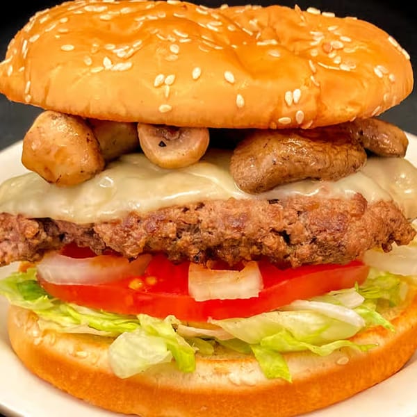 A Myra Jean's mushroom swiss burger with lettuce, tomato, and onion on a sesame seed bun.