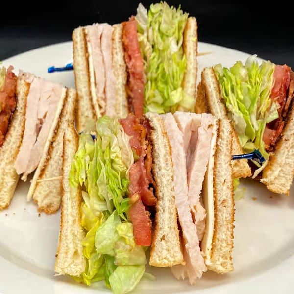 Four Myra Jean's club sandwiches, cut in halves, displaying turkey, bacon, lettuce, and tomato.