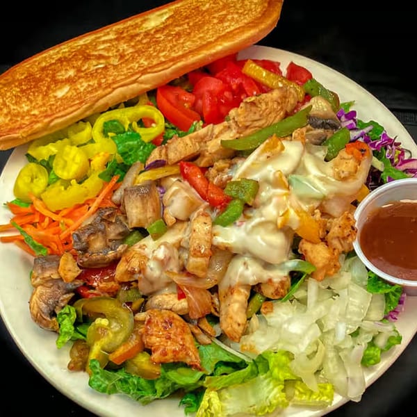 A Myra Jean's chicken cheesesteak salad with toasted bread, peppers, mushrooms, and dressing.