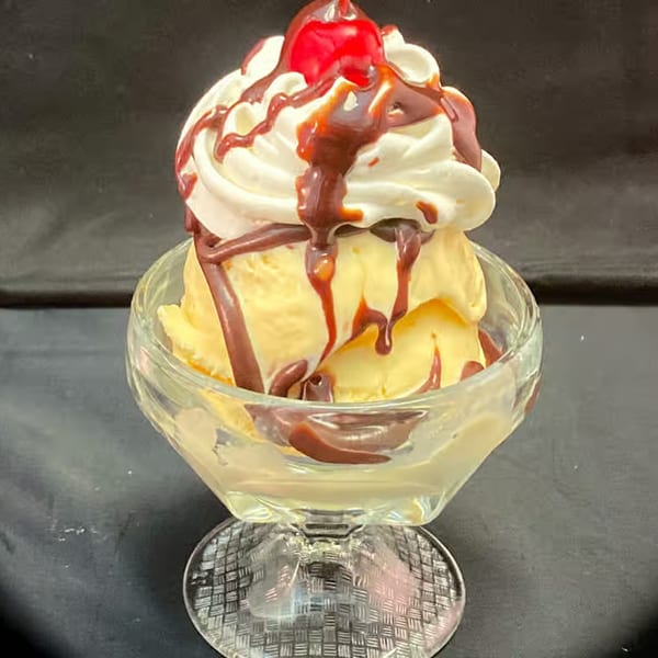 Vanilla ice cream sundae with whipped cream, chocolate syrup, and a cherry in a glass dish.