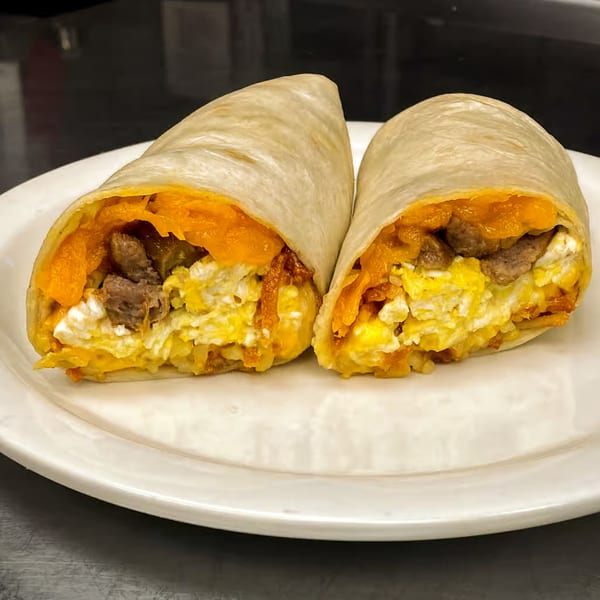 Two halves of a breakfast burrito filled with scrambled eggs, sausage, and shredded cheese on a white plate.